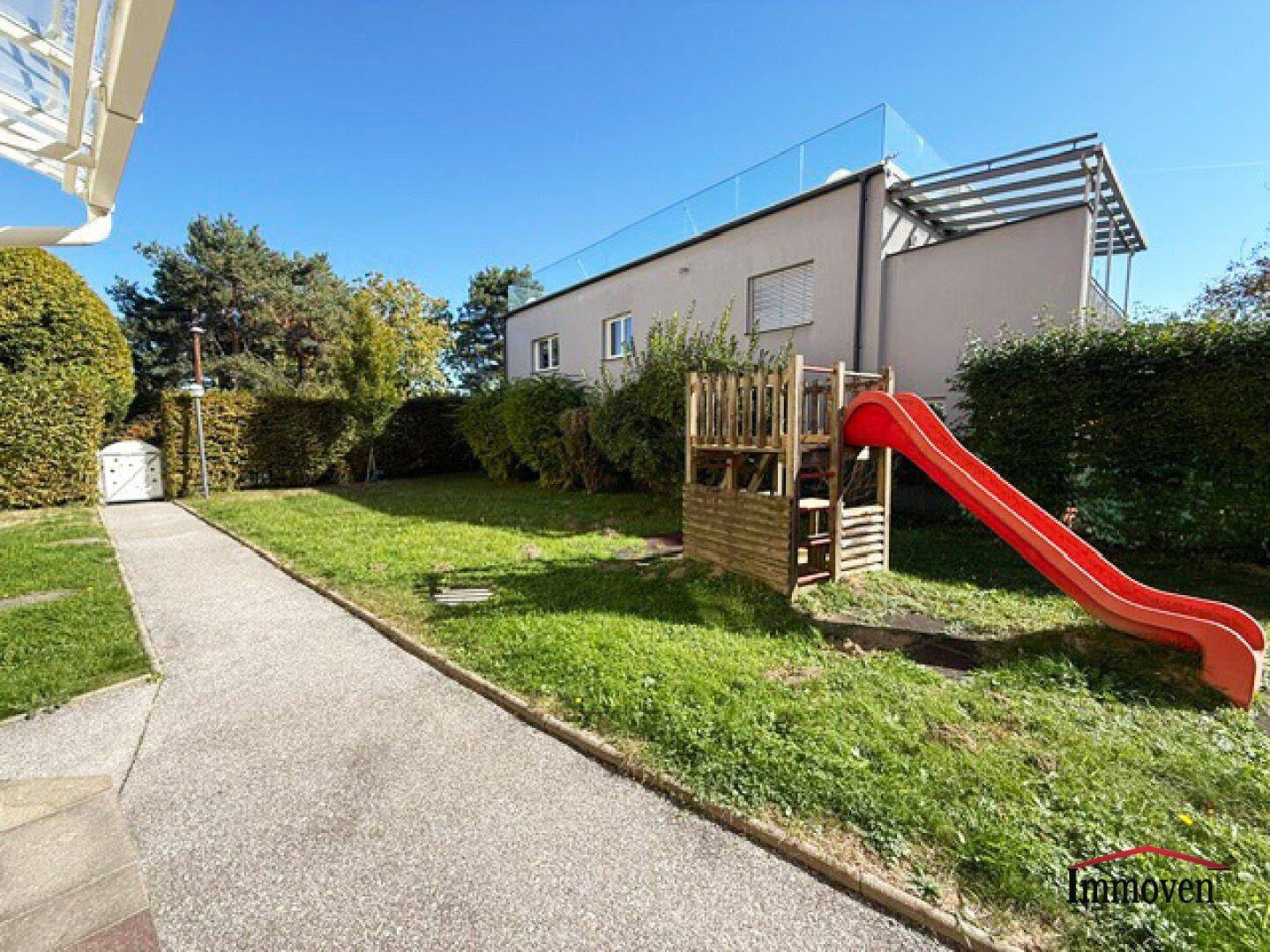 Sonniger Gartenbereich mit Kinderrutsche und gepflegter Hecke.