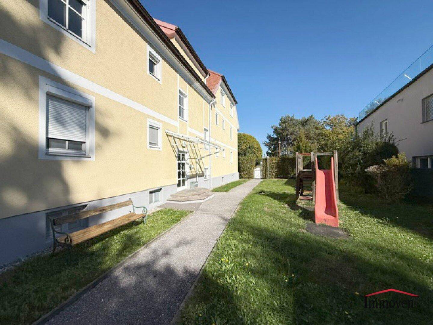 Außenansicht des Gebäudes mit Garten, Sitzbank und Kinderspielplatz.