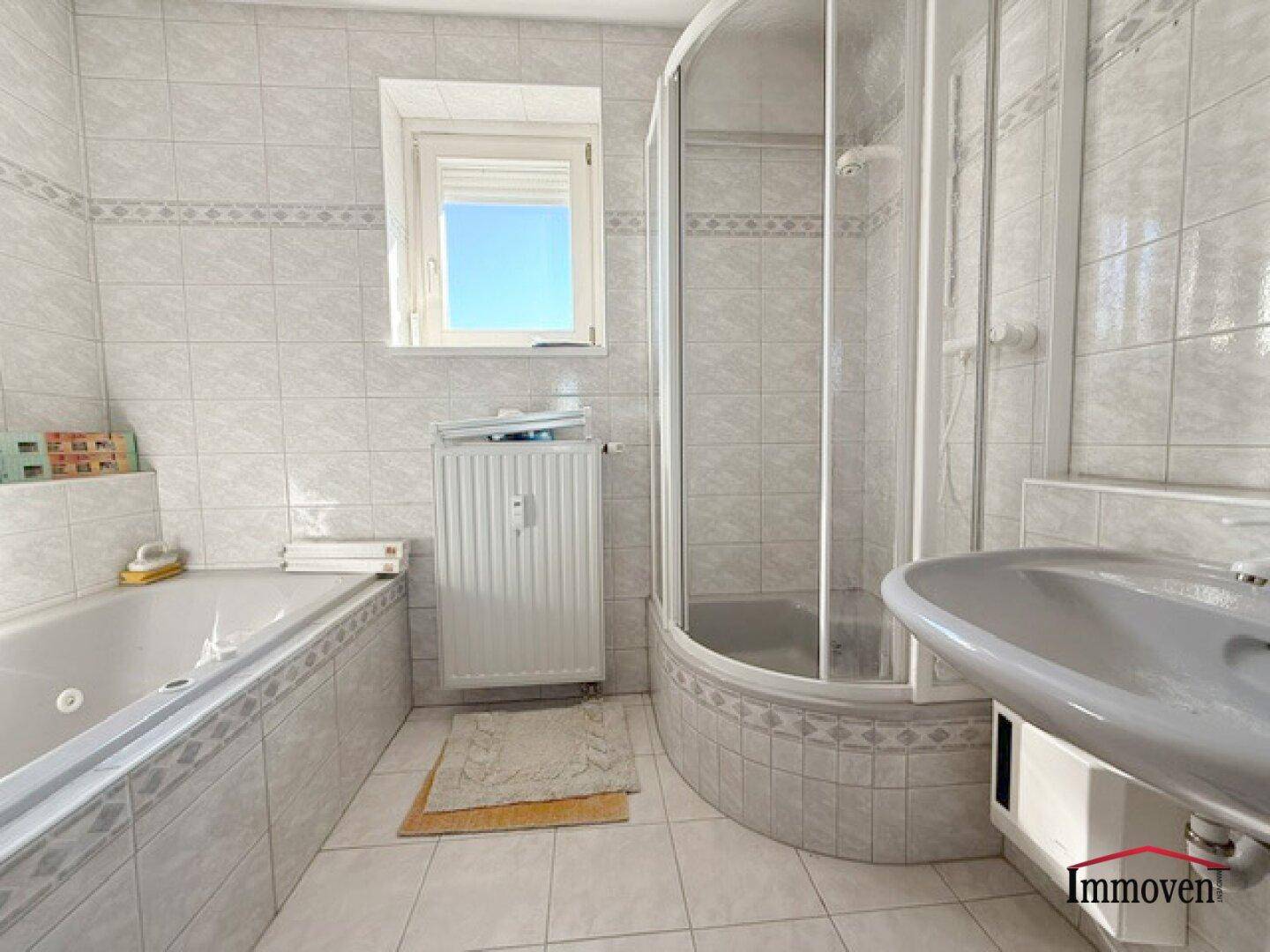 Gefliestes Badezimmer mit Badewanne, Duschkabine, Waschbecken und Fenster.