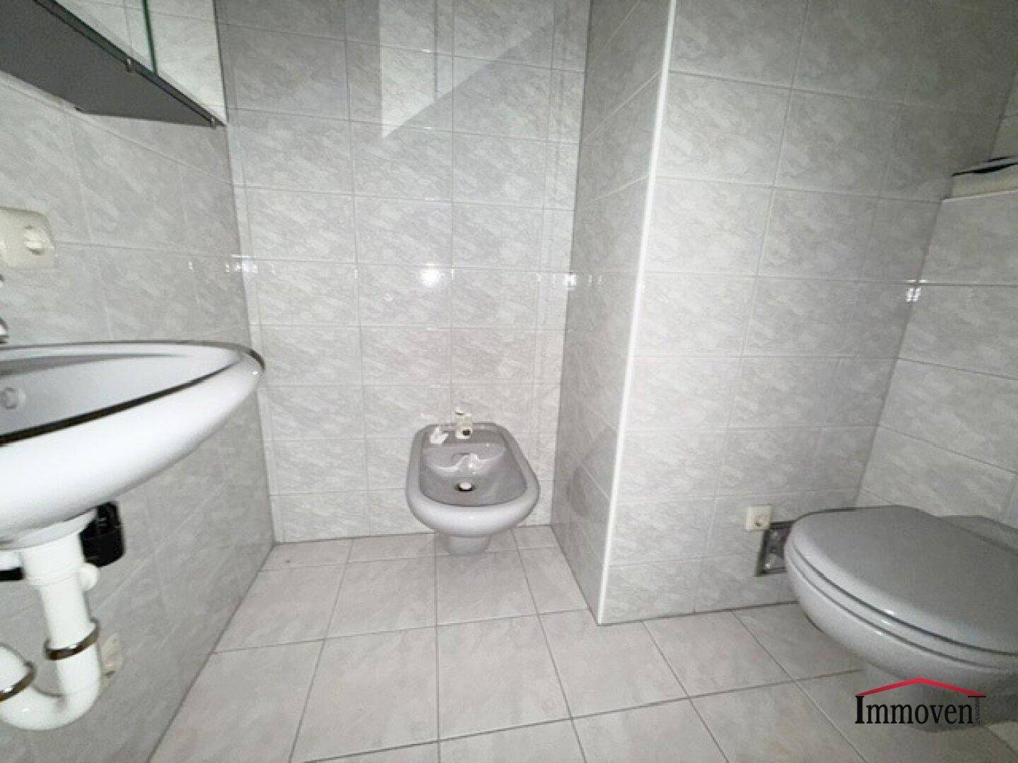 Kleines Badezimmer mit Bidet, Toilette und Waschbecken, komplett gefliest.
