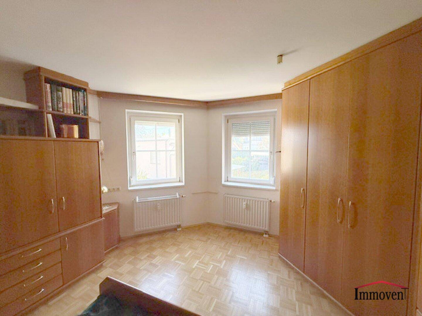 Schlafzimmer mit zwei Fenstern, Holzschränken und Parkettboden, bietet viel Stauraum.