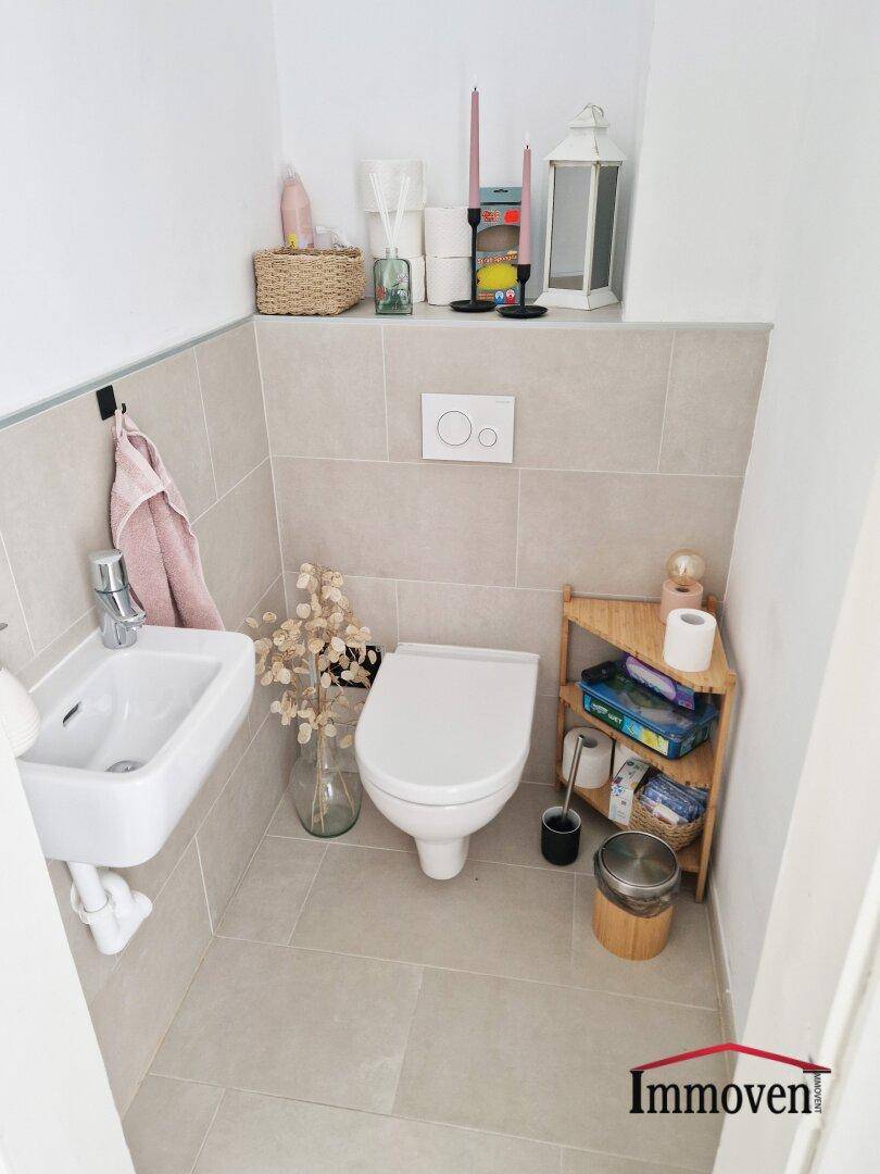 Kleines Gäste-WC mit Wand-WC, Handwaschbecken und hellen Fliesen.