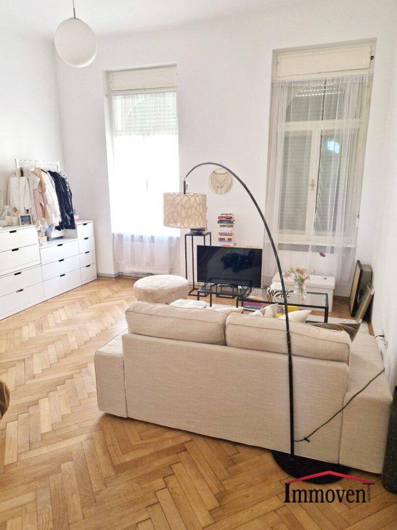 Helles Wohnzimmer mit Fischgrätparkett, beigem Sofa und modernen Möbeln.