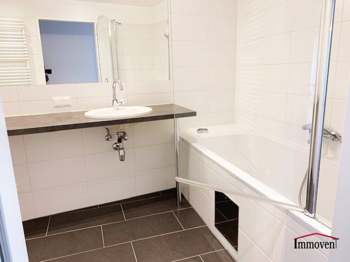 Modernes Badezimmer mit Badewanne, Duschabtrennung, Einzelwaschbecken und dunklen Fliesen.