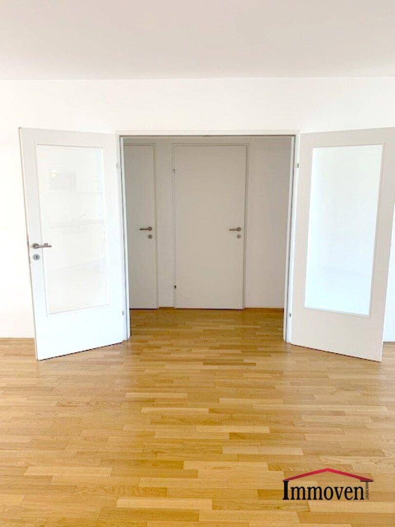 Heller Raum mit Parkettboden und zwei Glastüren, die zu weiteren Zimmern führen.