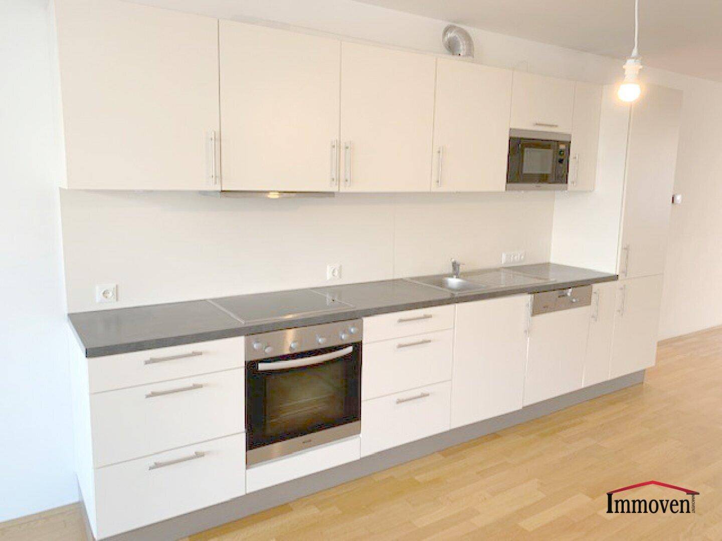 Moderne Einbauküche mit weißen Schränken, grauer Arbeitsplatte und integrierten Geräten.
