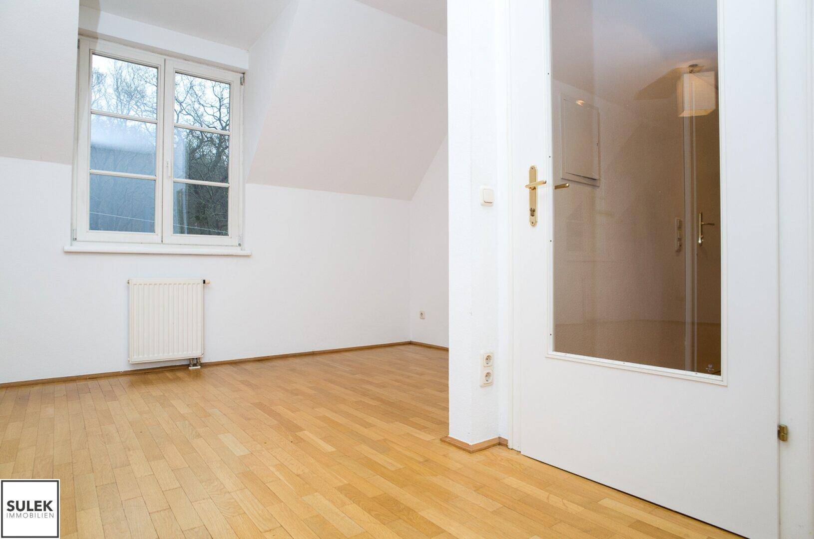 Geräumiges, helles Zimmer mit Parkettboden und Dachschrägen, durch eine Glastür zugänglich.