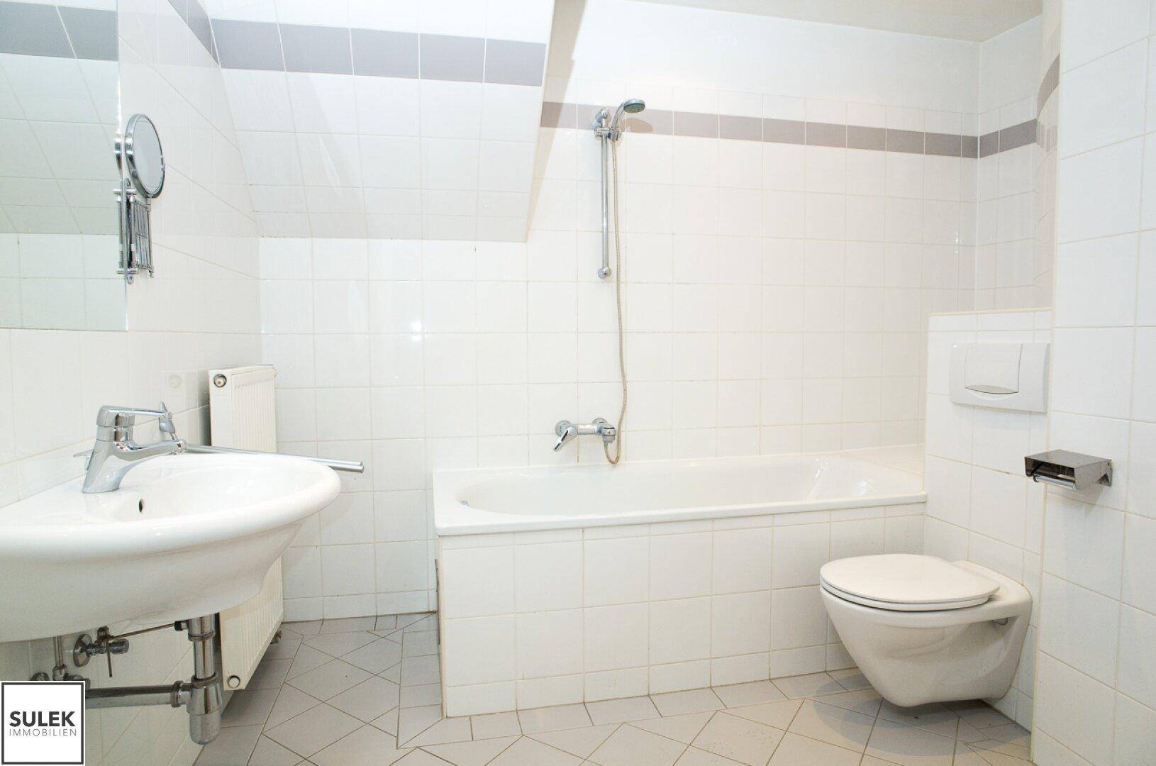 Gefliestes Badezimmer mit Badewanne, Waschbecken und wandhängendem WC, unter einer Dachschräge.