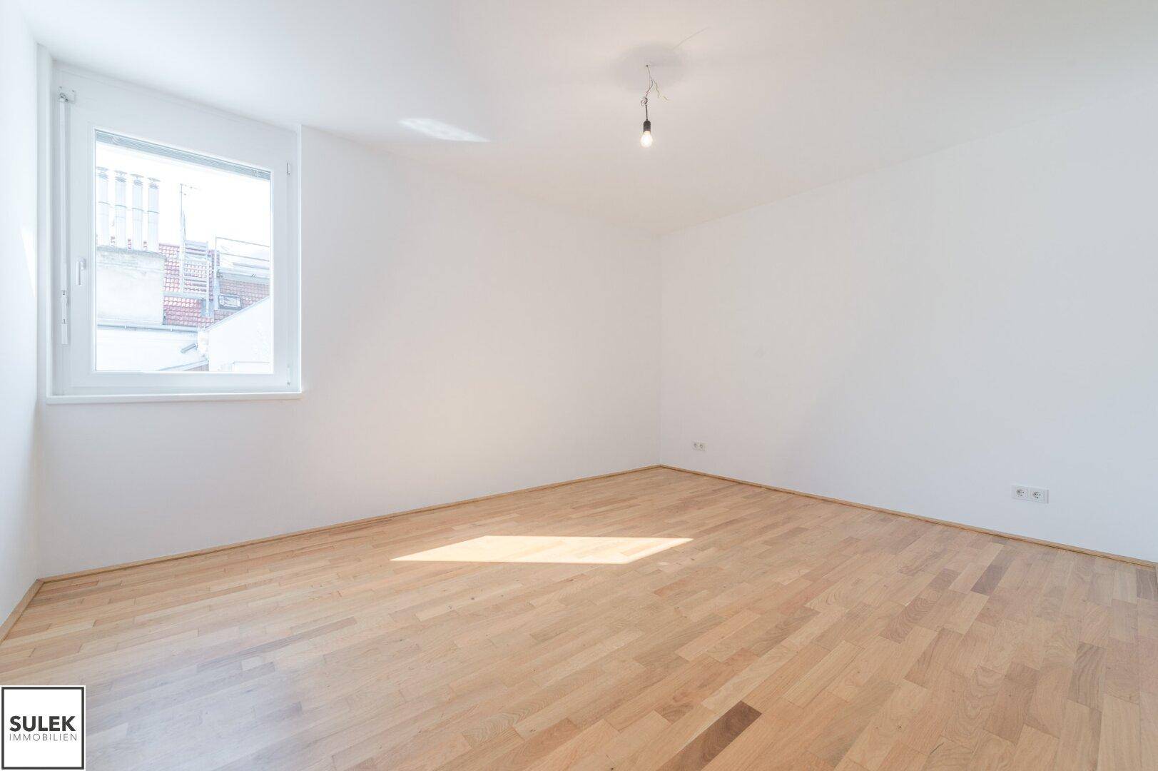 Helles, leeres Zimmer mit Holzboden und einem Fenster, ideal als Schlaf- oder Arbeitszimmer.