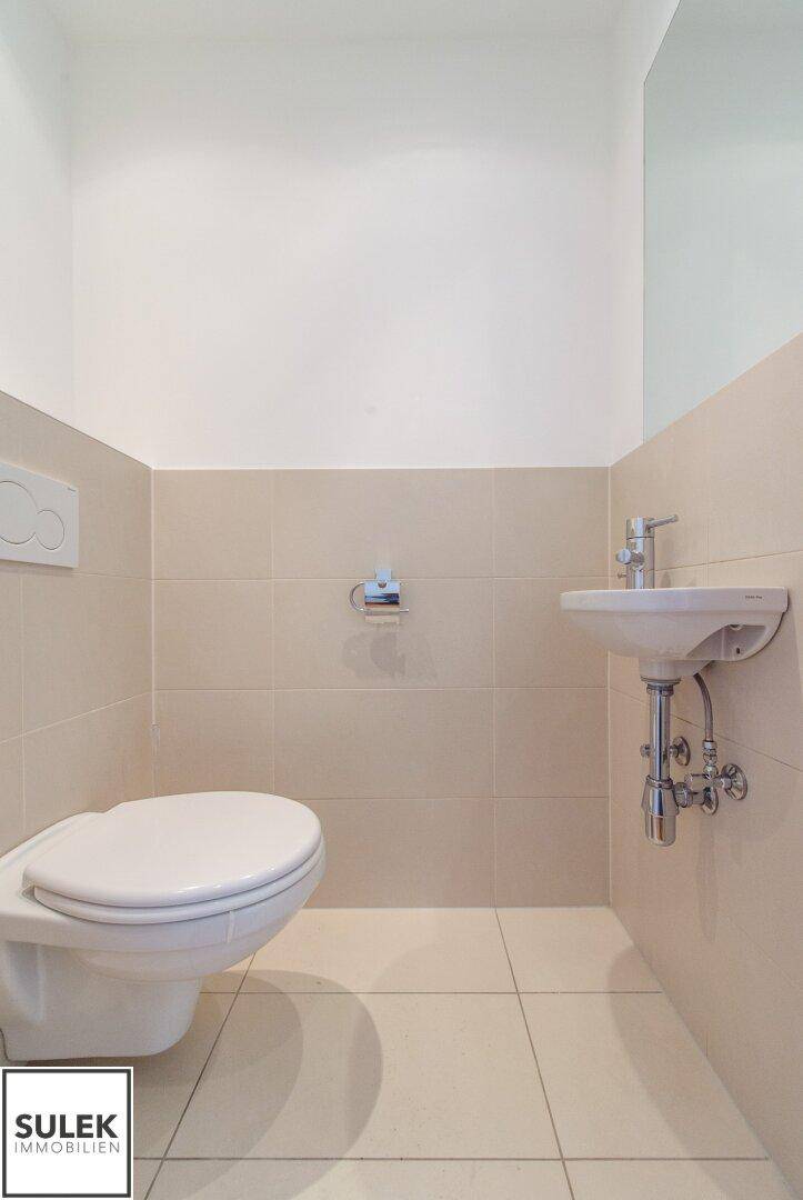 Separates Gäste-WC mit Wand-WC, kleinem Waschbecken und hellen Fliesen.