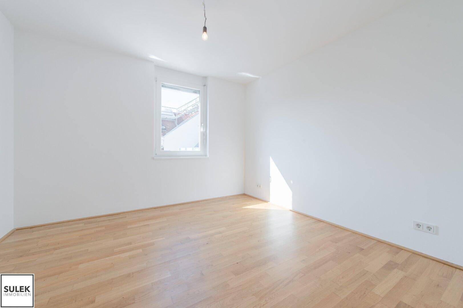 Lichtdurchflutetes Zimmer mit Holzboden und einem Fenster, bereit zur individuellen Gestaltung.