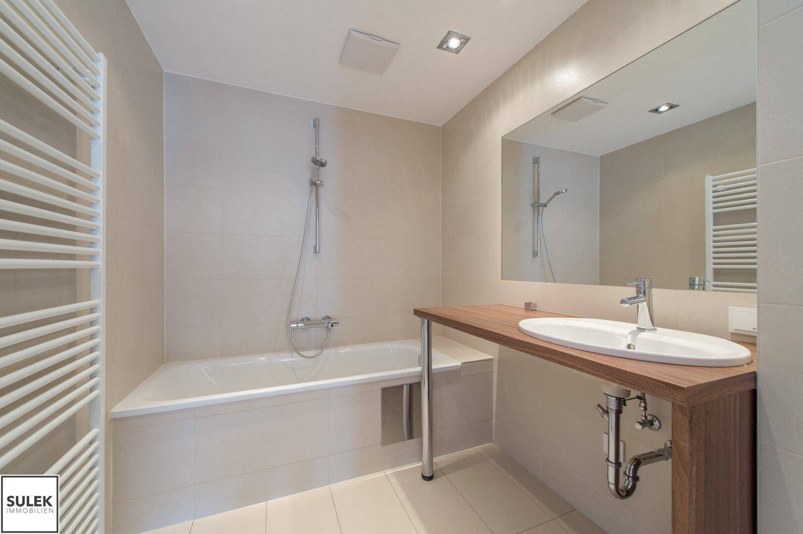 Modernes Badezimmer mit Badewanne, Einzelwaschbecken und beheiztem Handtuchhalter.