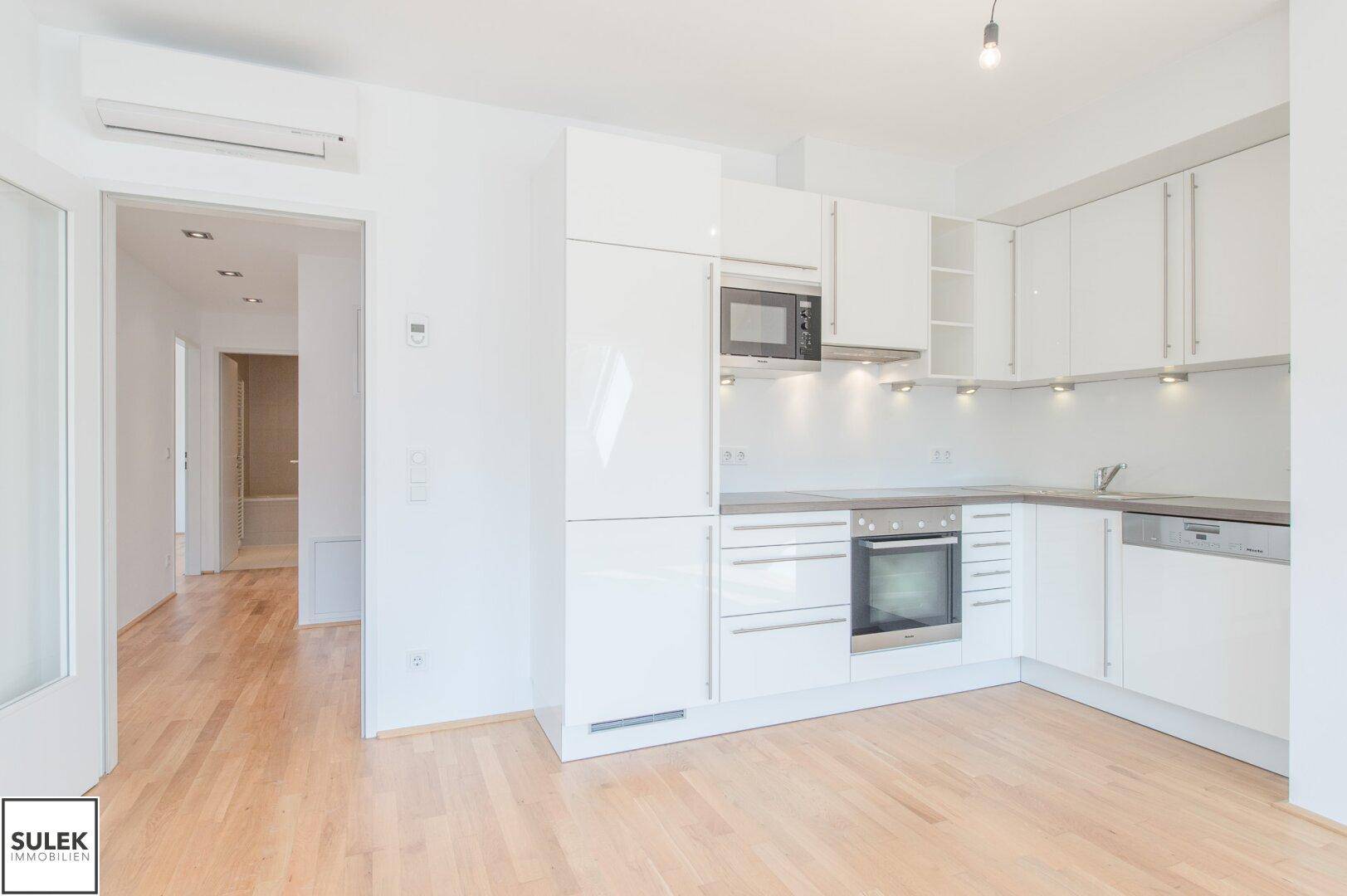Moderne Einbauküche mit weißen Hochglanzfronten, integrierten Geräten und Holzboden.