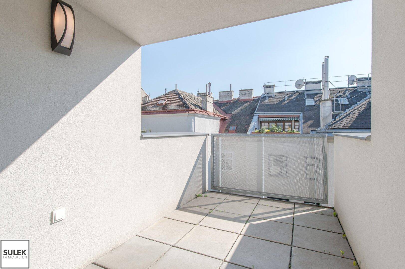 Sonniger Außenbereich mit Fliesenboden und Blick auf die umliegenden Dächer.