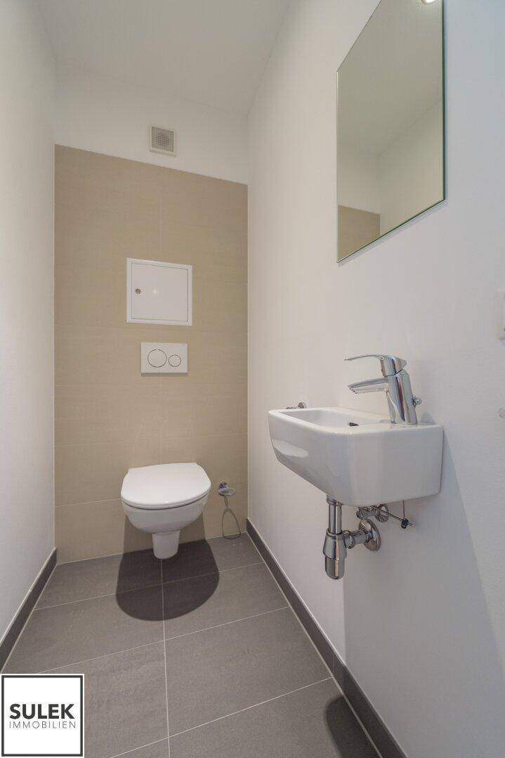 Helles Gäste-WC mit Wand-WC, kleinem Waschbecken und modernem Spiegel.