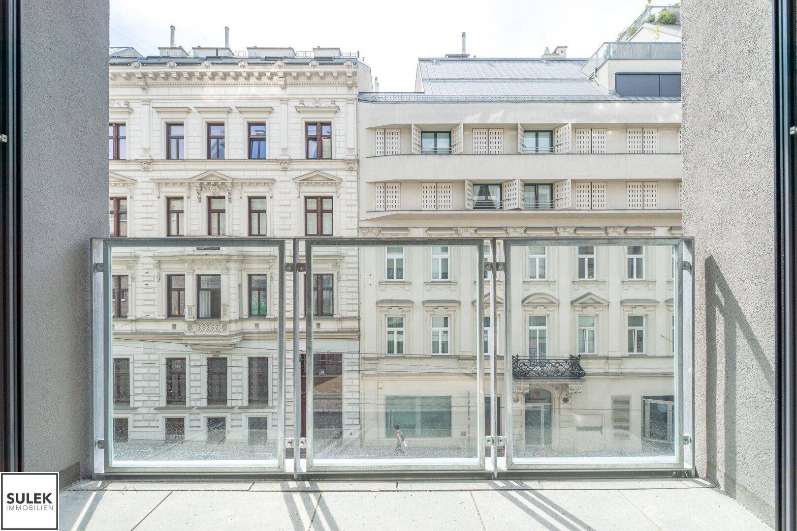 Balkon mit Glasbrüstung und Blick auf die gegenüberliegenden historischen Gebäude.