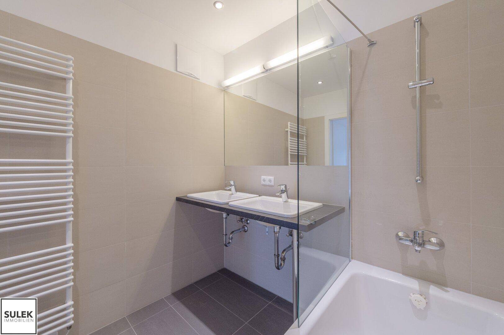 Modernes Badezimmer mit Doppelwaschbecken, Badewanne und beheiztem Handtuchhalter.