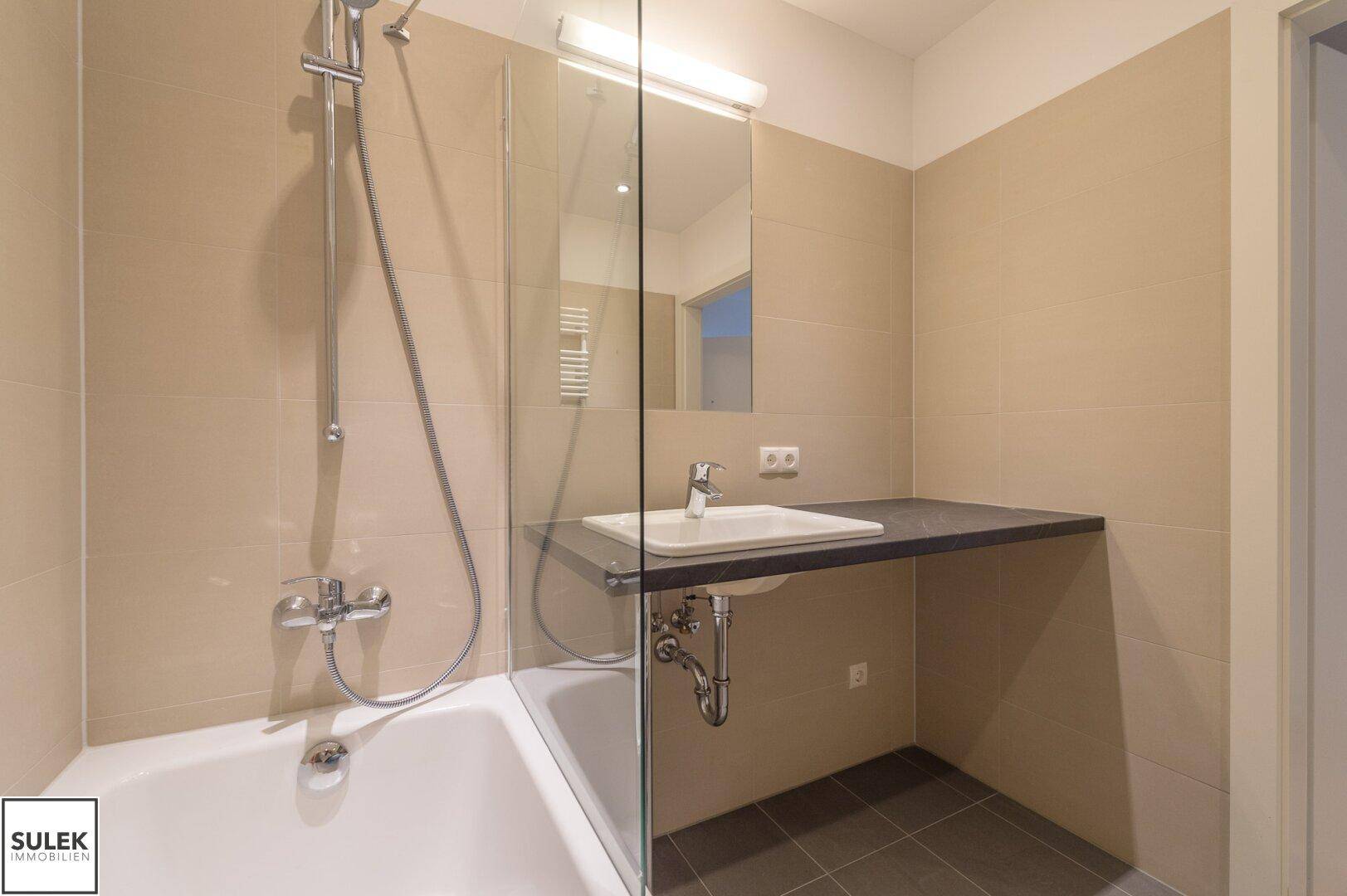 Helles Badezimmer mit Badewanne, Duschfunktion und modernem Waschtisch mit Spiegel.