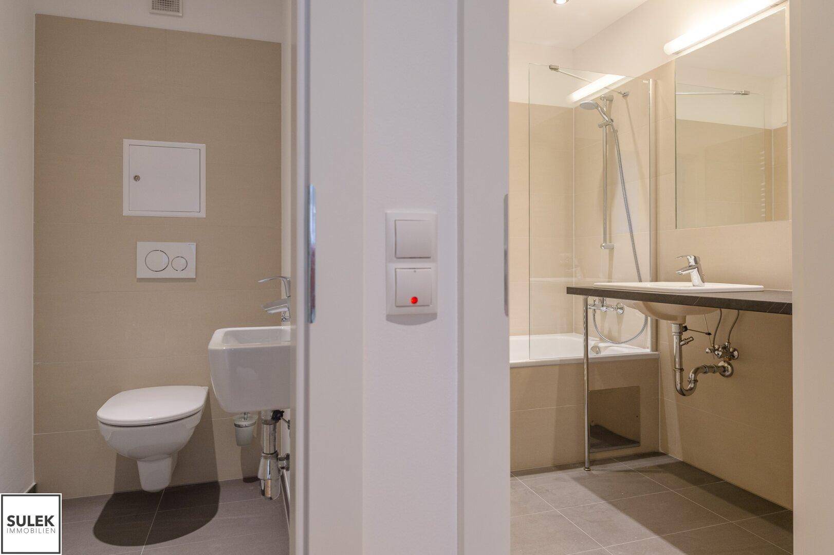 Blick vom Flur in das separate Gäste-WC und das Hauptbadezimmer mit Badewanne.