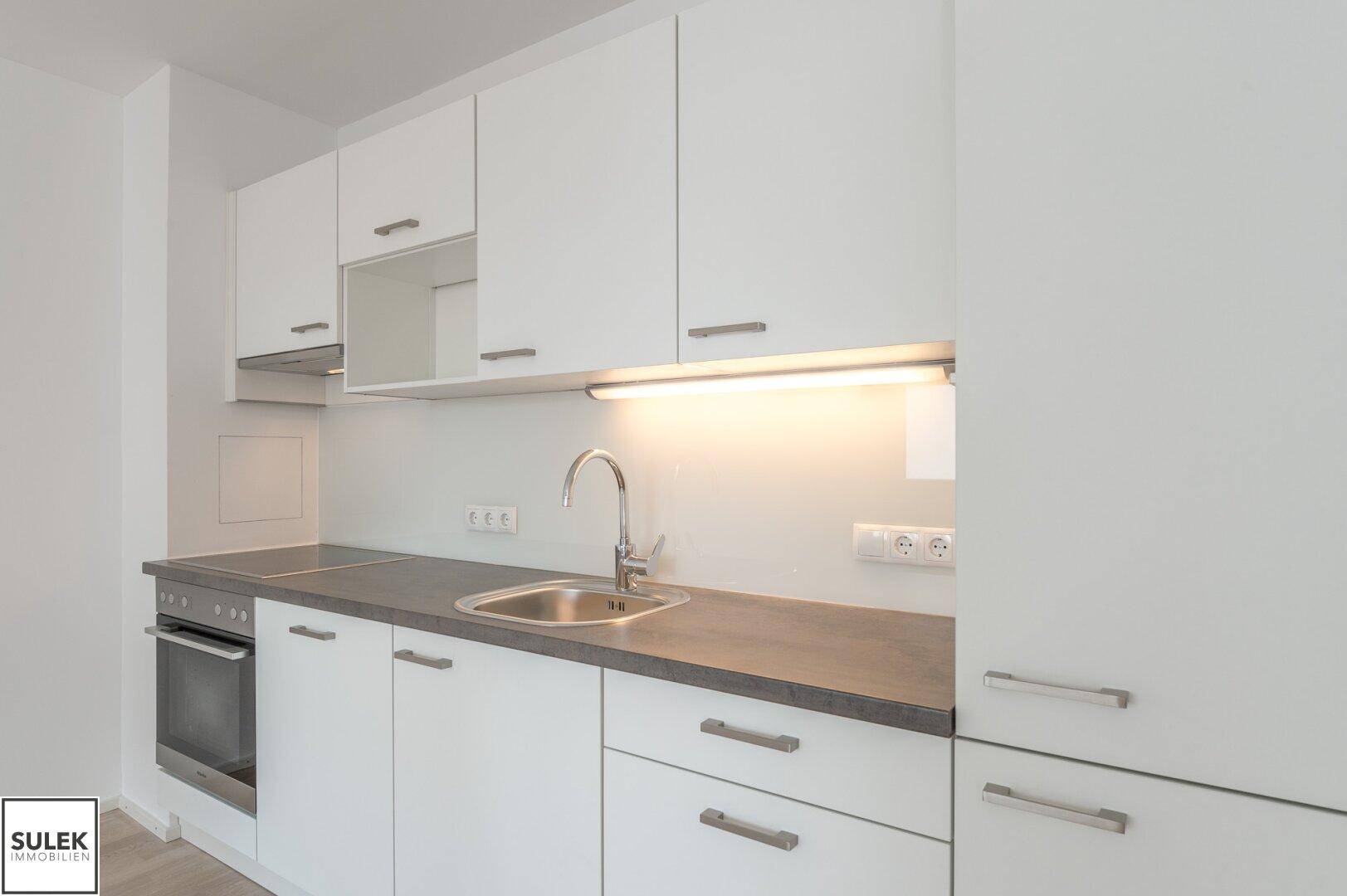 Moderne Küchenzeile mit weißen Schränken, dunkler Arbeitsplatte und integriertem Backofen.