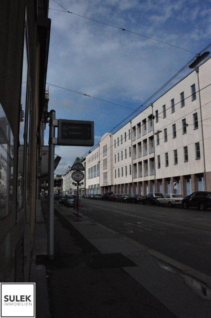Eine ruhige Stadtstraße mit geparkten Autos und mehrstöckigen Wohngebäuden unter einem bewölkten Himmel.
