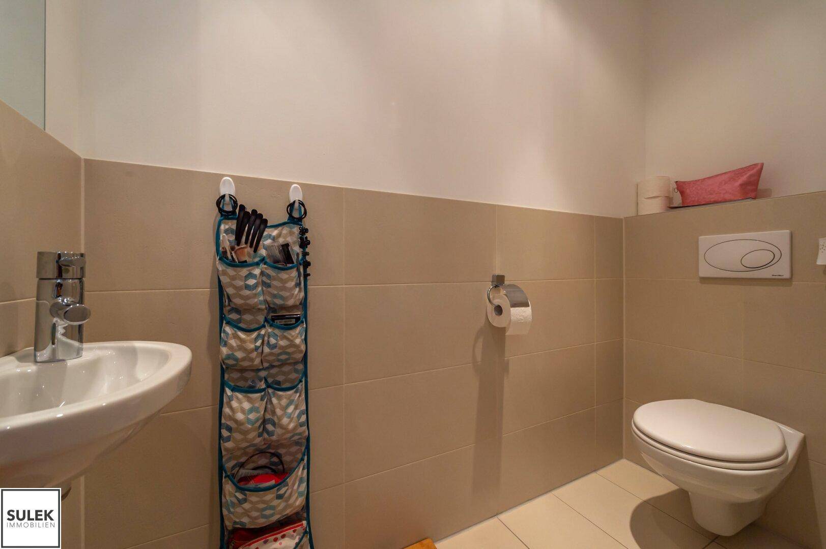 Separates Gäste-WC mit Wand-WC und kleinem Waschbecken, hell gefliest.