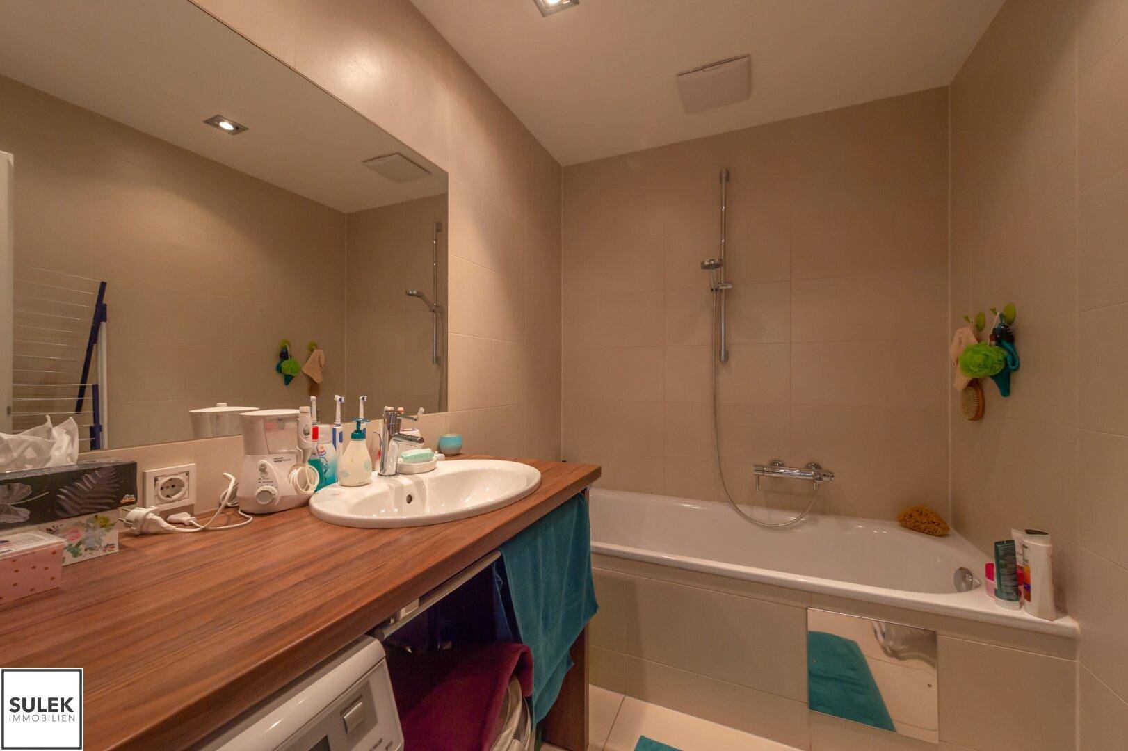 Modernes Badezimmer mit Badewanne, integrierter Dusche und Waschbecken mit Holzunterschrank.