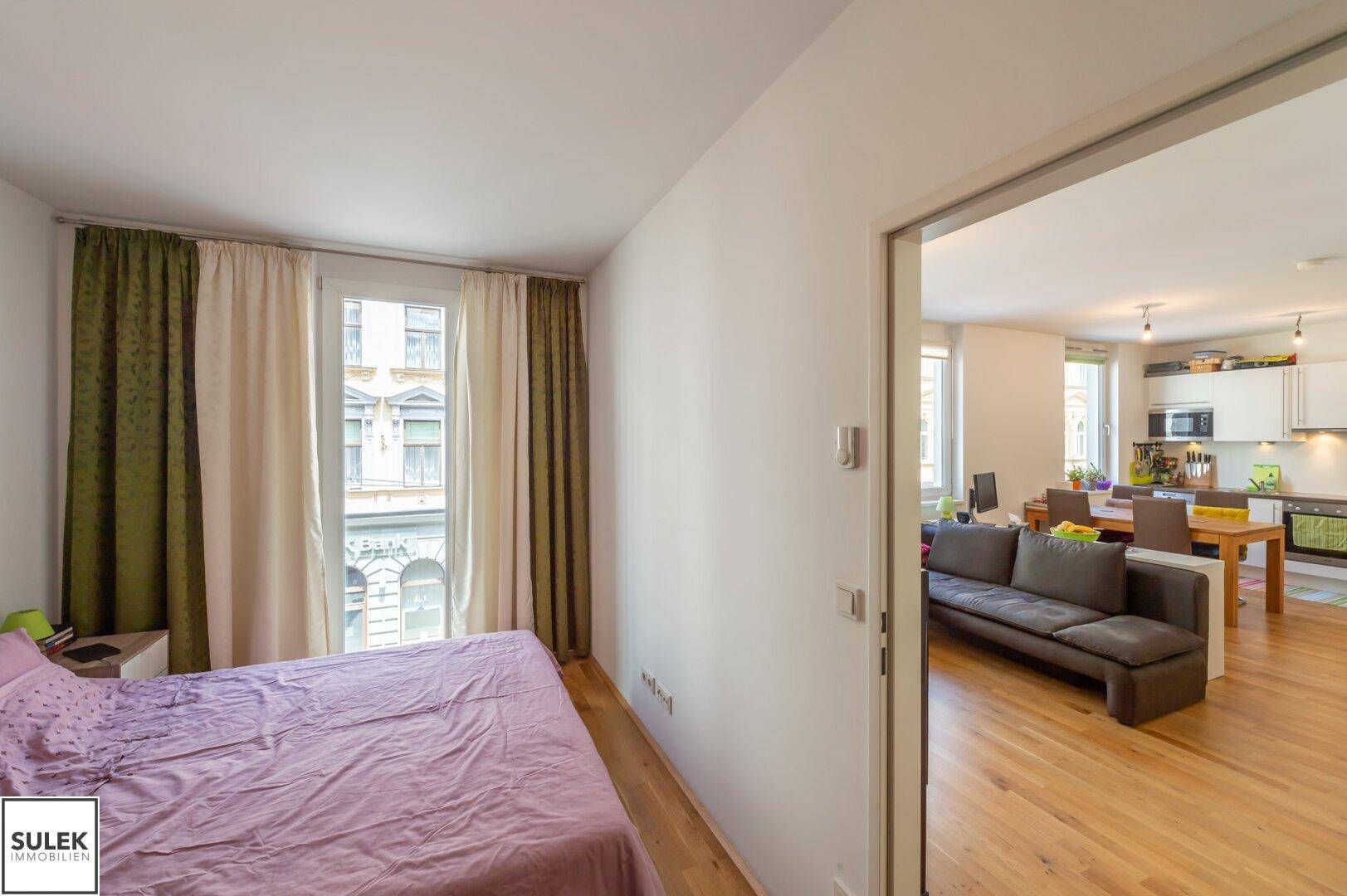 Schlafzimmer mit Blick auf den offenen Wohn- und Küchenbereich, ausgestattet mit Holzboden.