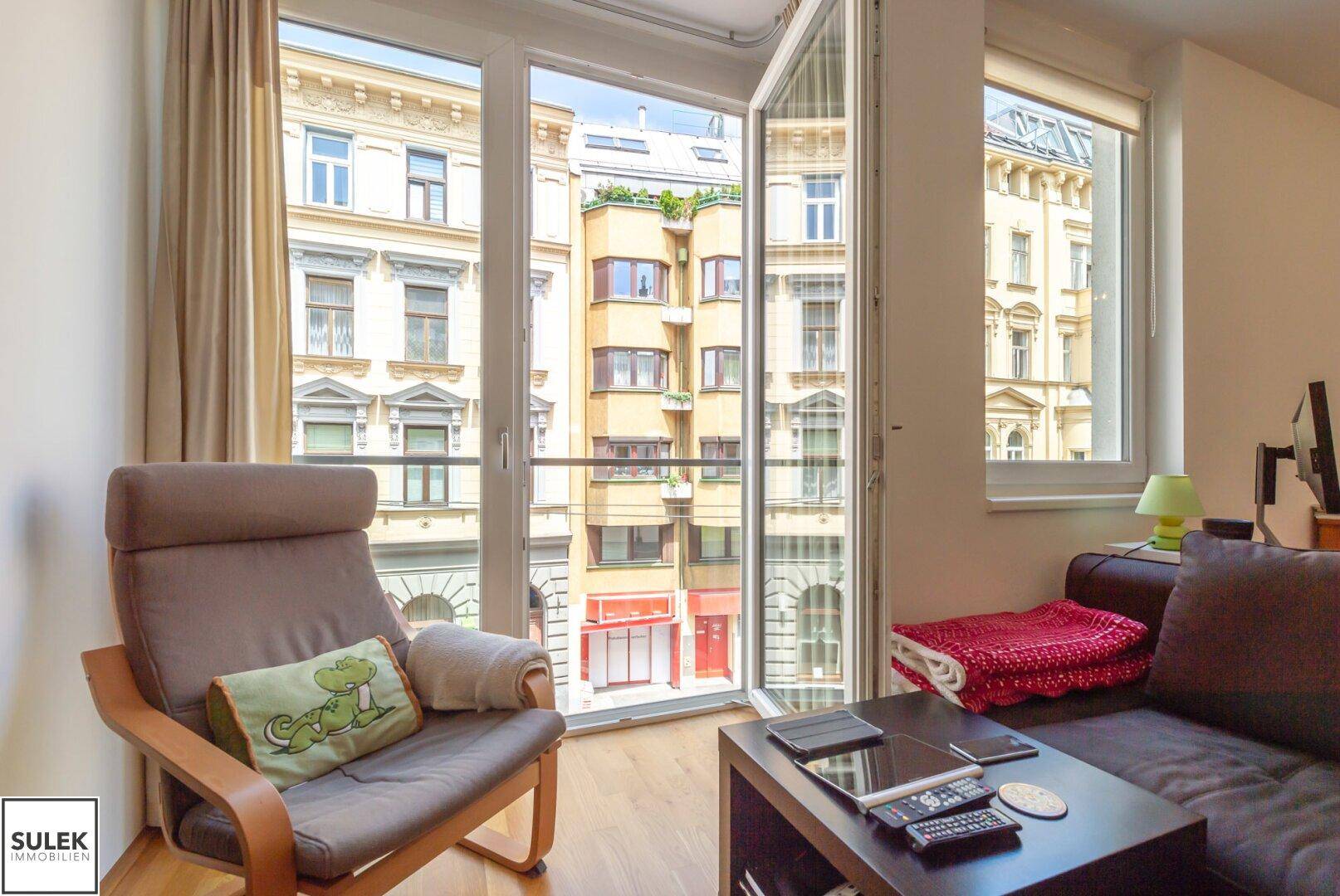 Gemütlicher Wohnbereich mit Sessel und Sofa, bietet einen Blick auf die umliegenden Stadtgebäude.