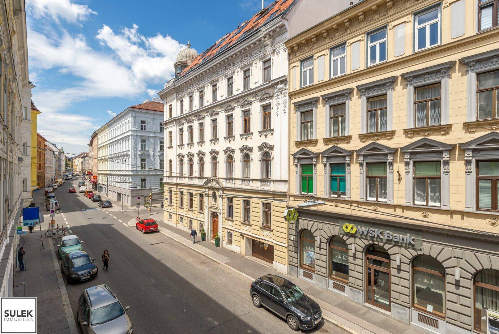 Blick auf eine belebte Stadtstraße mit historischen Gebäuden und Geschäften unter blauem Himmel.