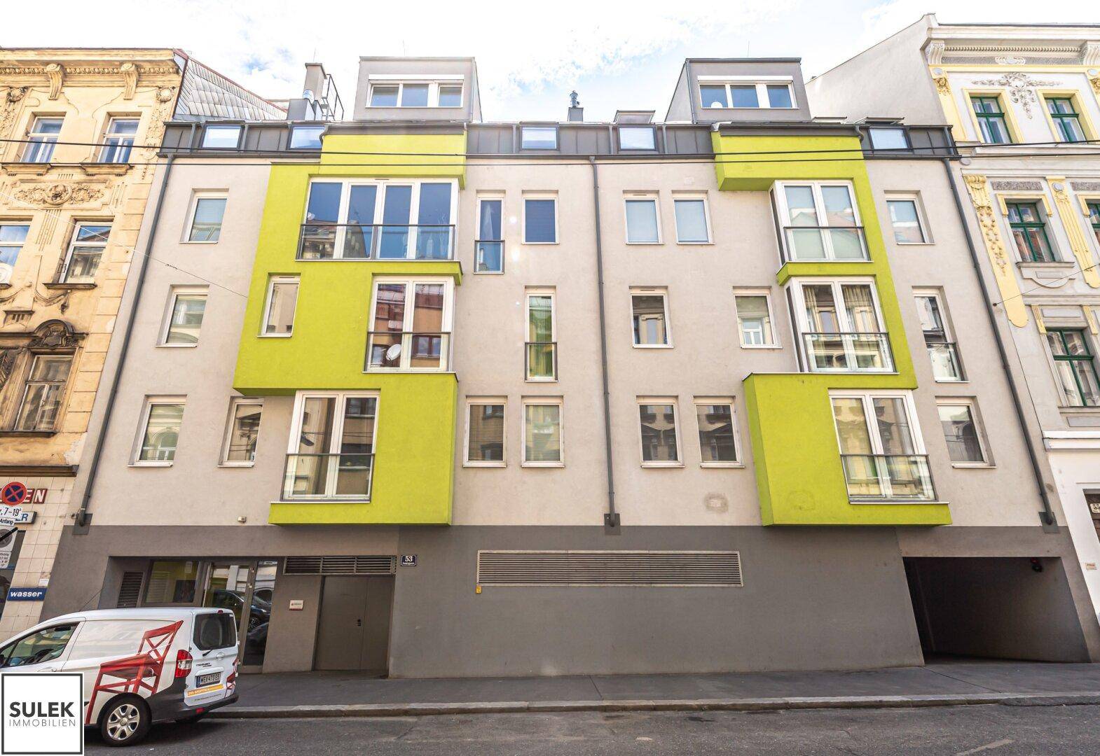 Moderne Gebäudefassade mit leuchtend grünen Akzenten und großen Fenstern in städtischer Umgebung.