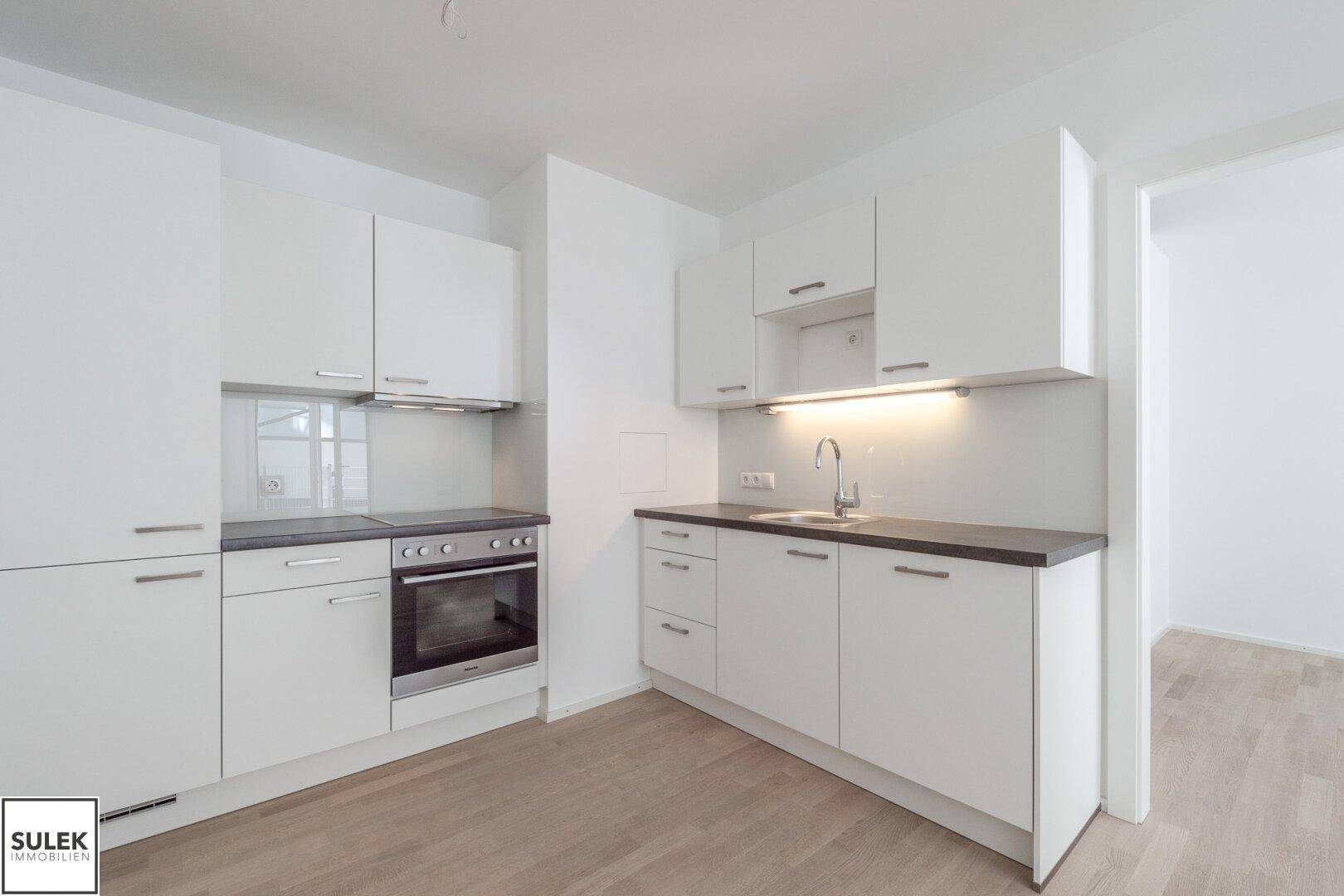 Moderne Küchenzeile mit weißen Schränken, dunkler Arbeitsplatte und integriertem Backofen, in neuwertigem Zustand.