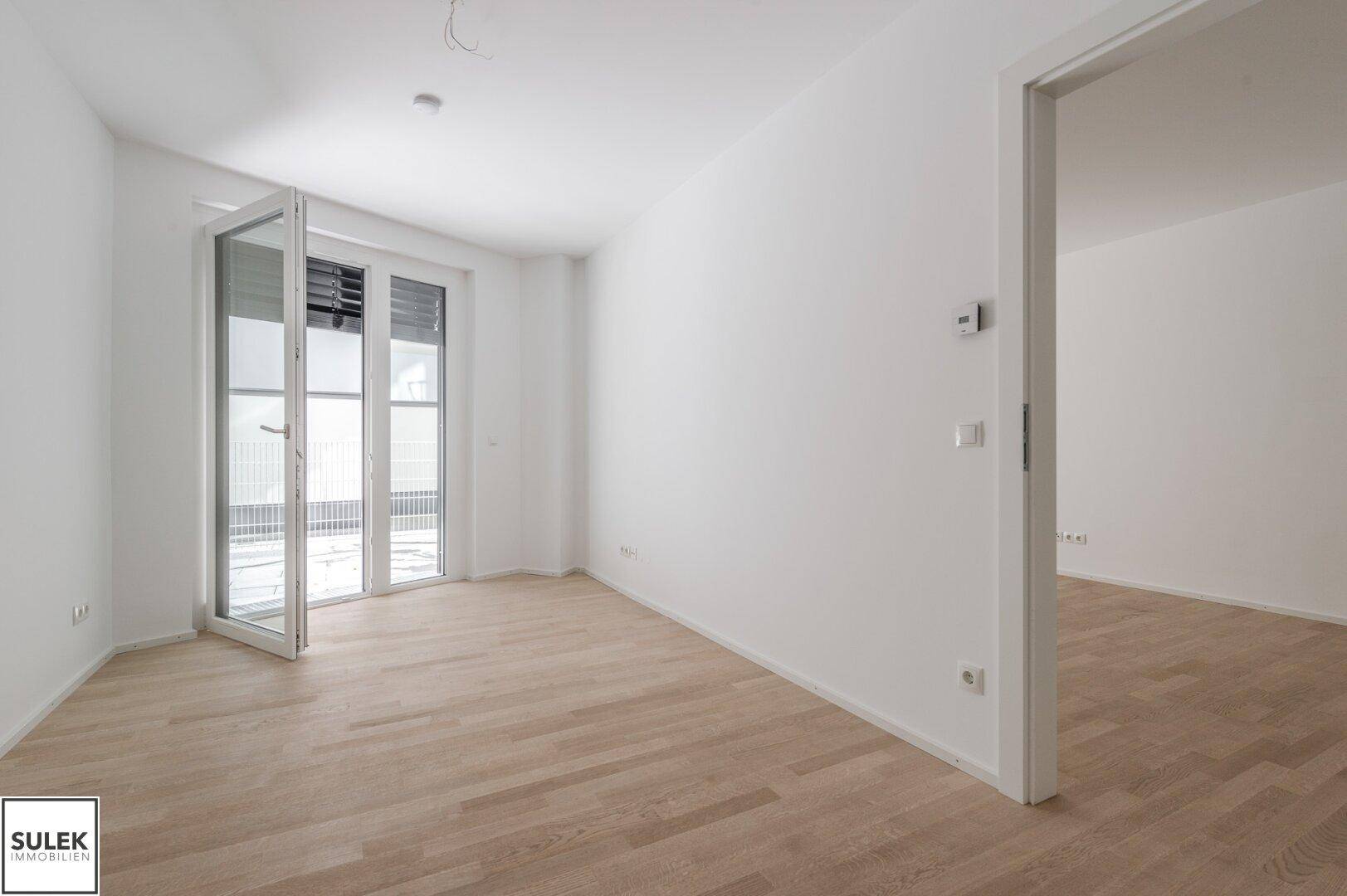Helles Zimmer mit Parkettboden und Zugang zu einem Außenbereich, ausgestattet mit modernen Rollläden.