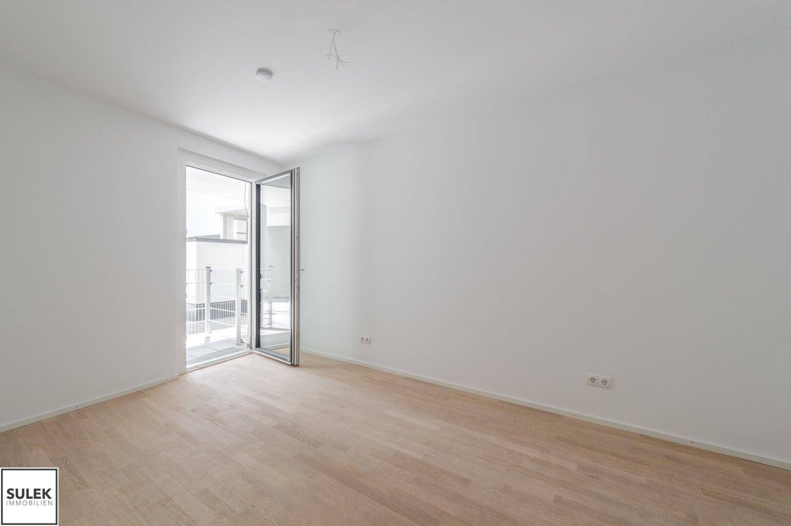 Helles, leeres Zimmer mit hellem Parkettboden und Zugang zu einem Balkon, bereit zur individuellen Gestaltung.