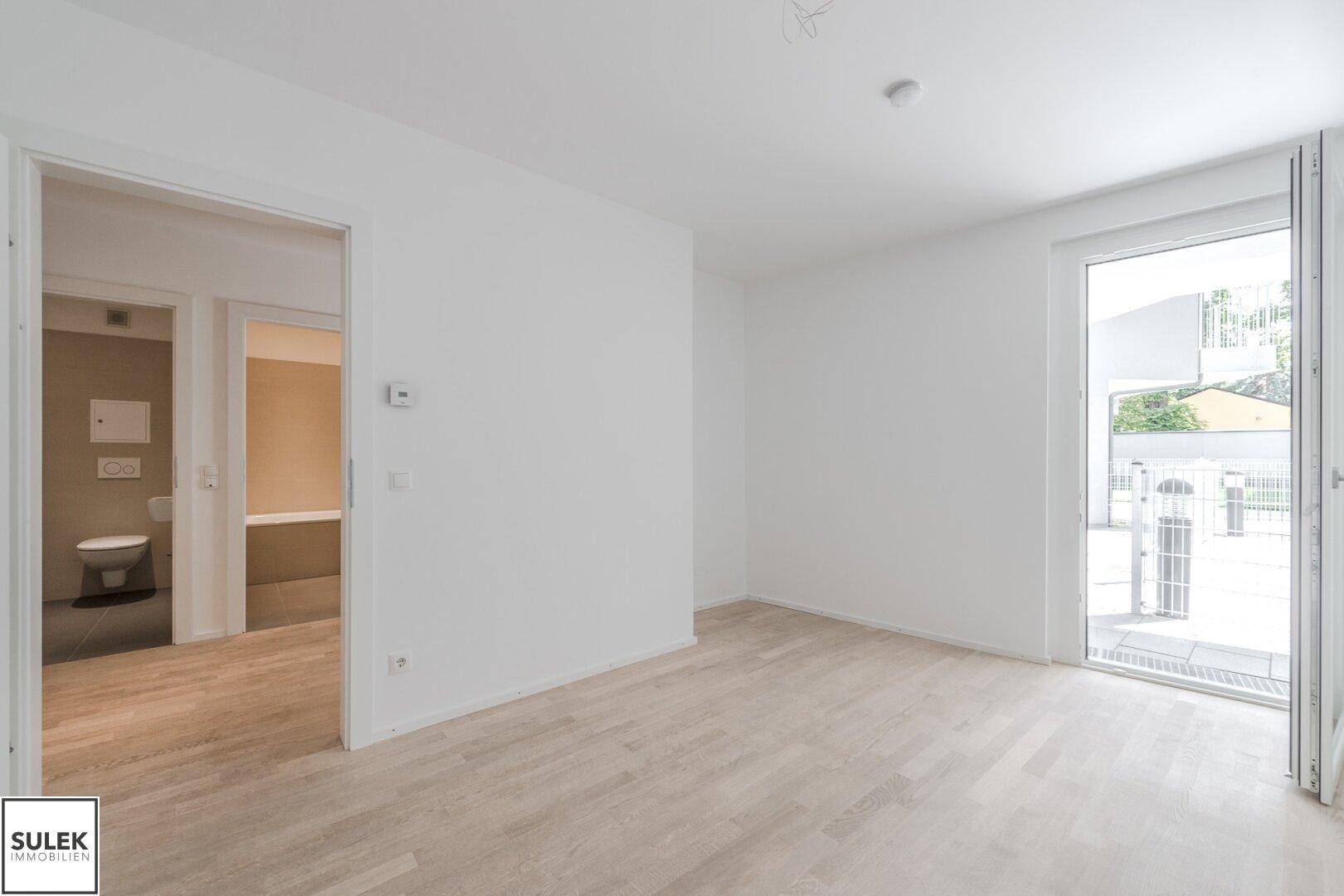 Helles Zimmer mit Parkettboden und Zugang zu einem Außenbereich sowie einem modernen Badezimmer.