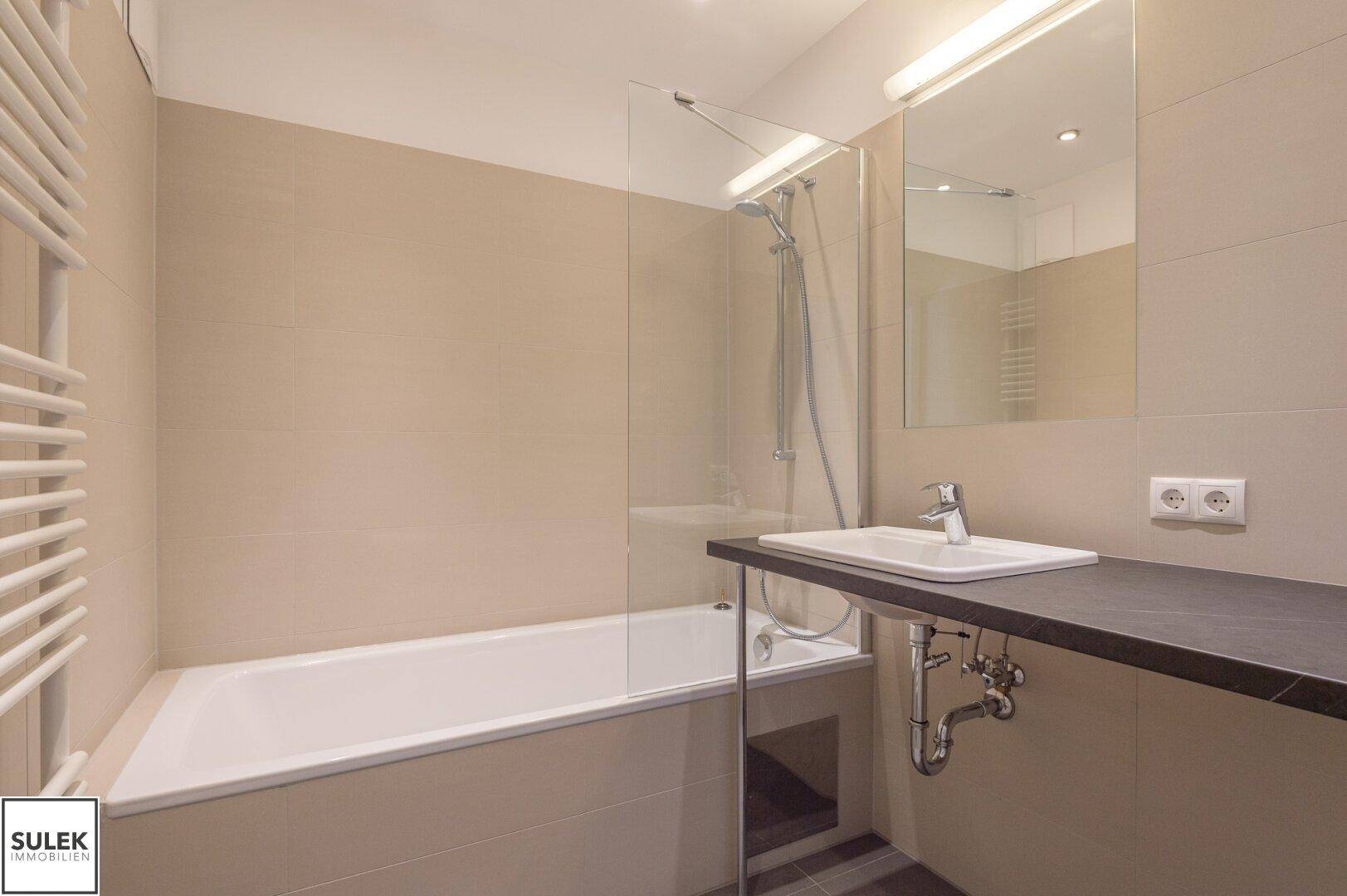 Modernes Badezimmer mit Badewanne, Duschfunktion, Waschbecken und beheiztem Handtuchhalter, in neutralen Tönen.