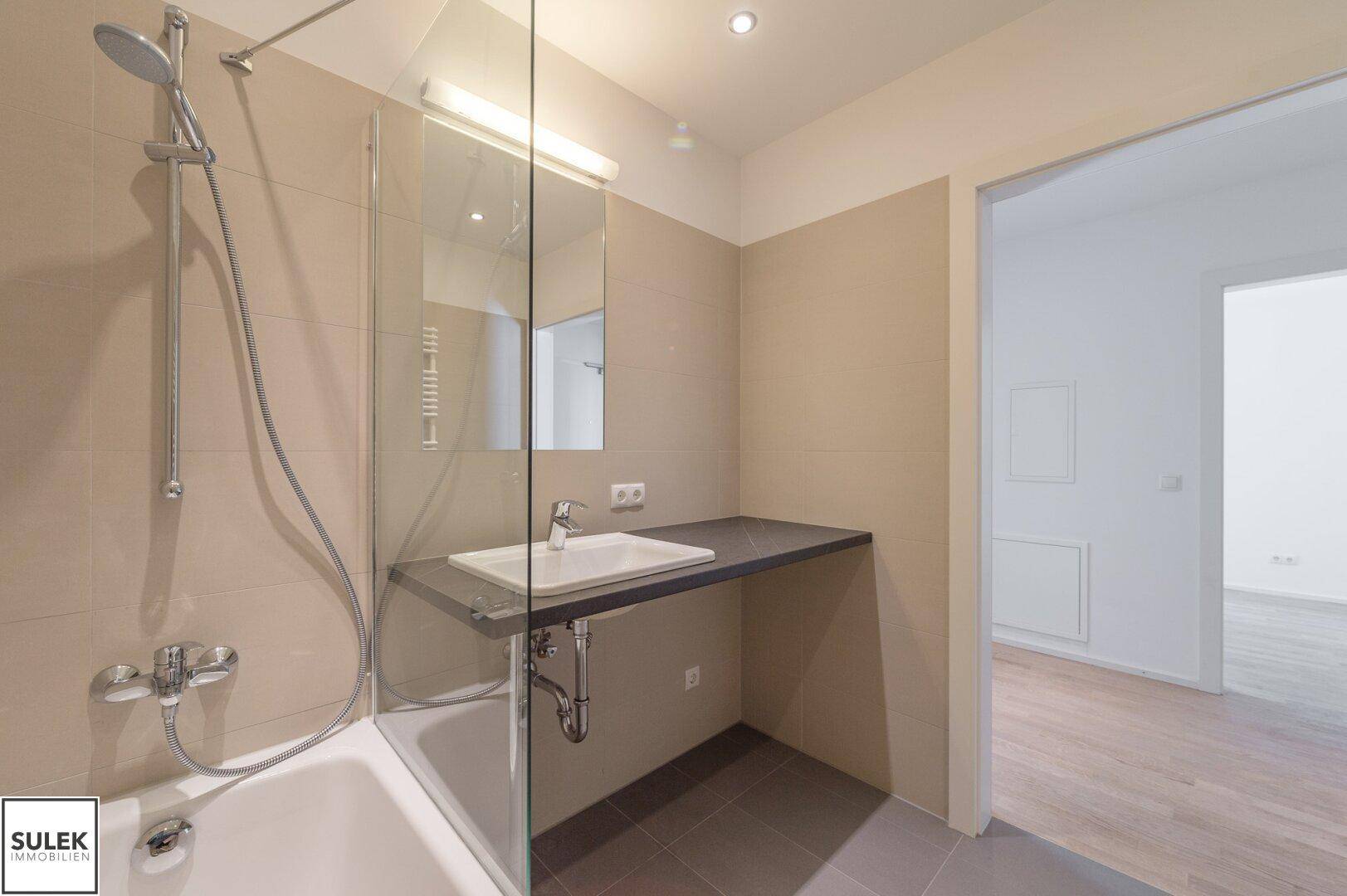 Helles Badezimmer mit Badewanne, Duschabtrennung, Waschbecken und beheiztem Handtuchhalter, funktional und sauber.