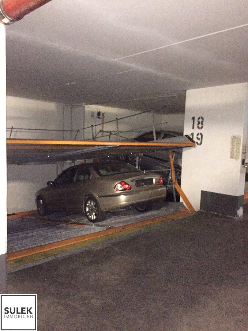 Tiefgarage mit einem Auto auf einer unteren Parkplattform eines Doppelparkers, umgeben von Betonwänden.