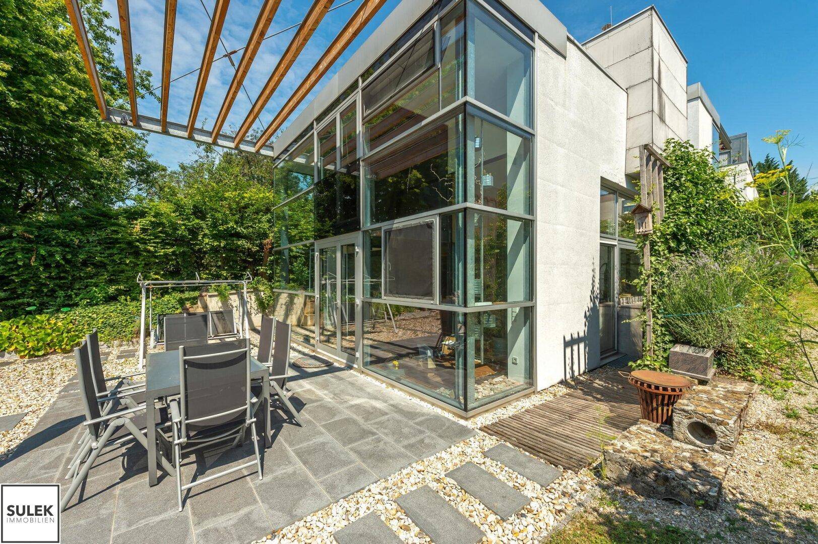 Geräumige Terrasse mit Gartenmöbeln und Schaukelstuhl vor der modernen Glasfassade des Hauses.