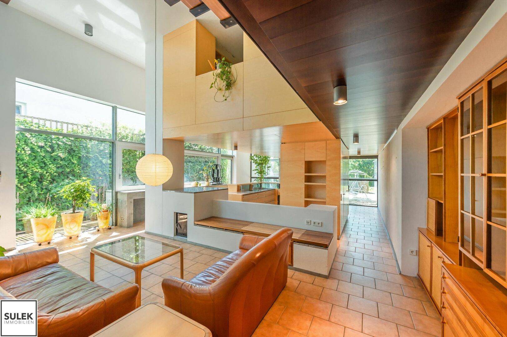 Helles Wohnzimmer mit hohen Decken, Ledersofas, Fliesenboden und Blick in den grünen Garten.