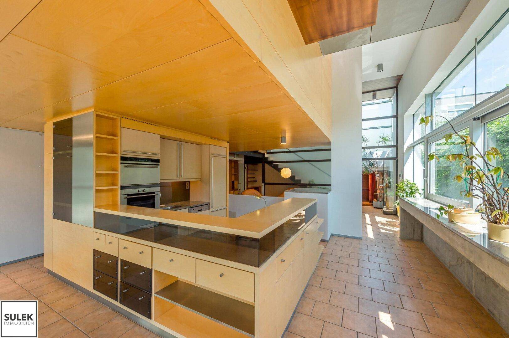 Offene Küche mit Holzschränken, Granitarbeitsplatte und Blick auf den Wohnbereich und die Treppe.