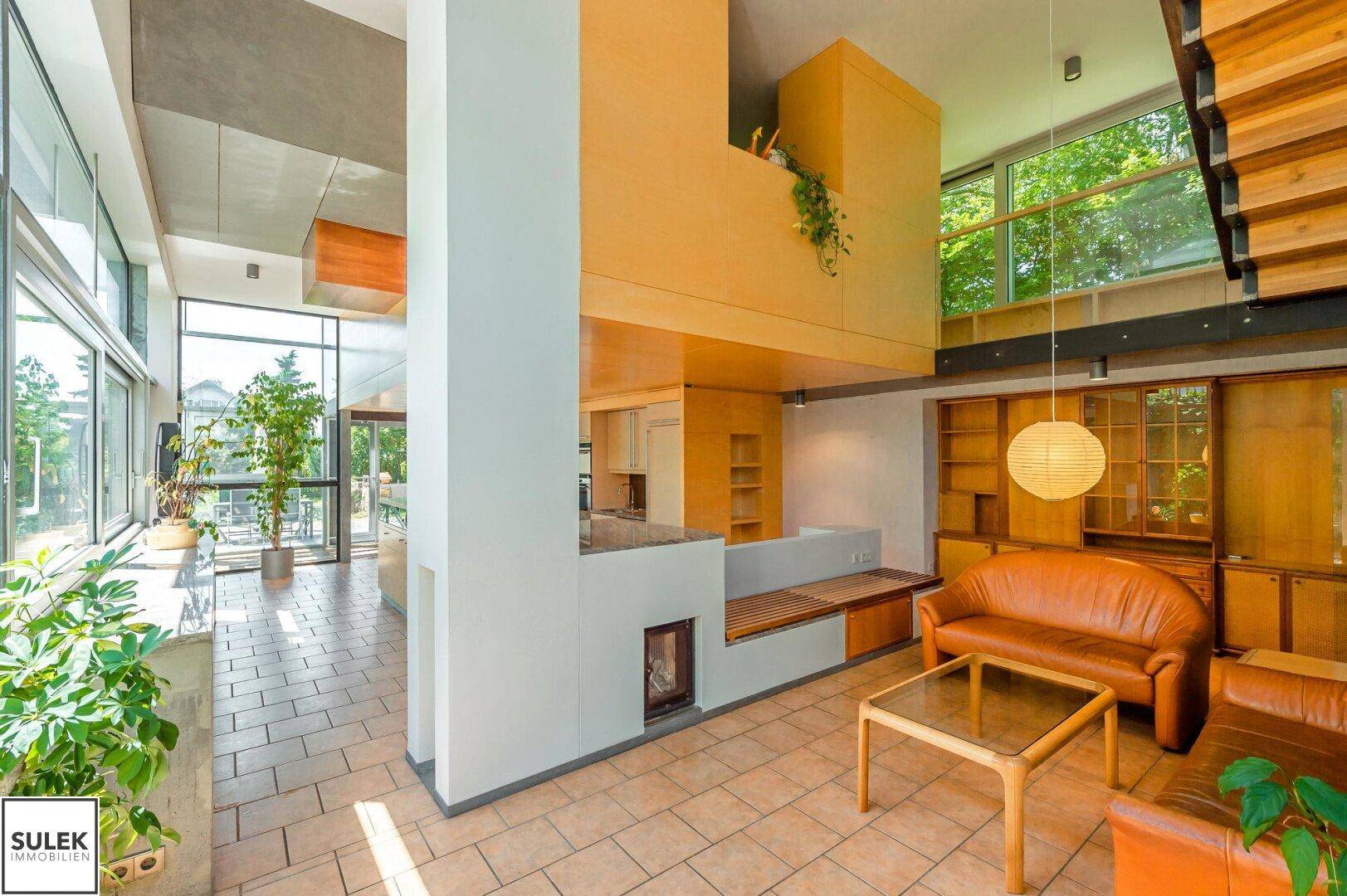 Geräumiges Wohnzimmer mit hohen Decken, Ledersofas, Kamin und Blick auf den Garten.