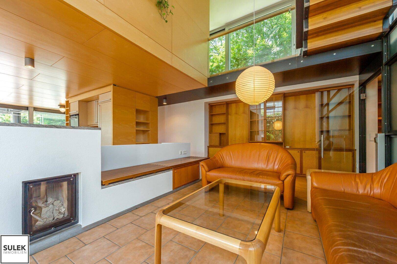 Gemütliches Wohnzimmer mit Ledersofas, Kamin und hohen Decken, offen zur Küche.