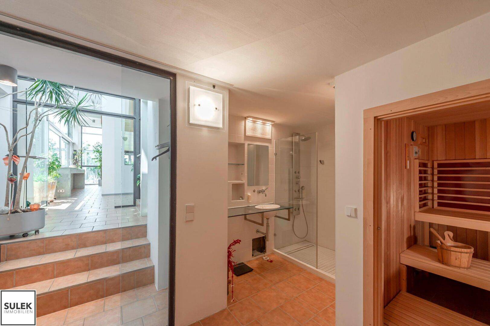 Badezimmer mit Dusche, Waschbecken und direktem Zugang zur Holzsauna, ideal für Entspannung.