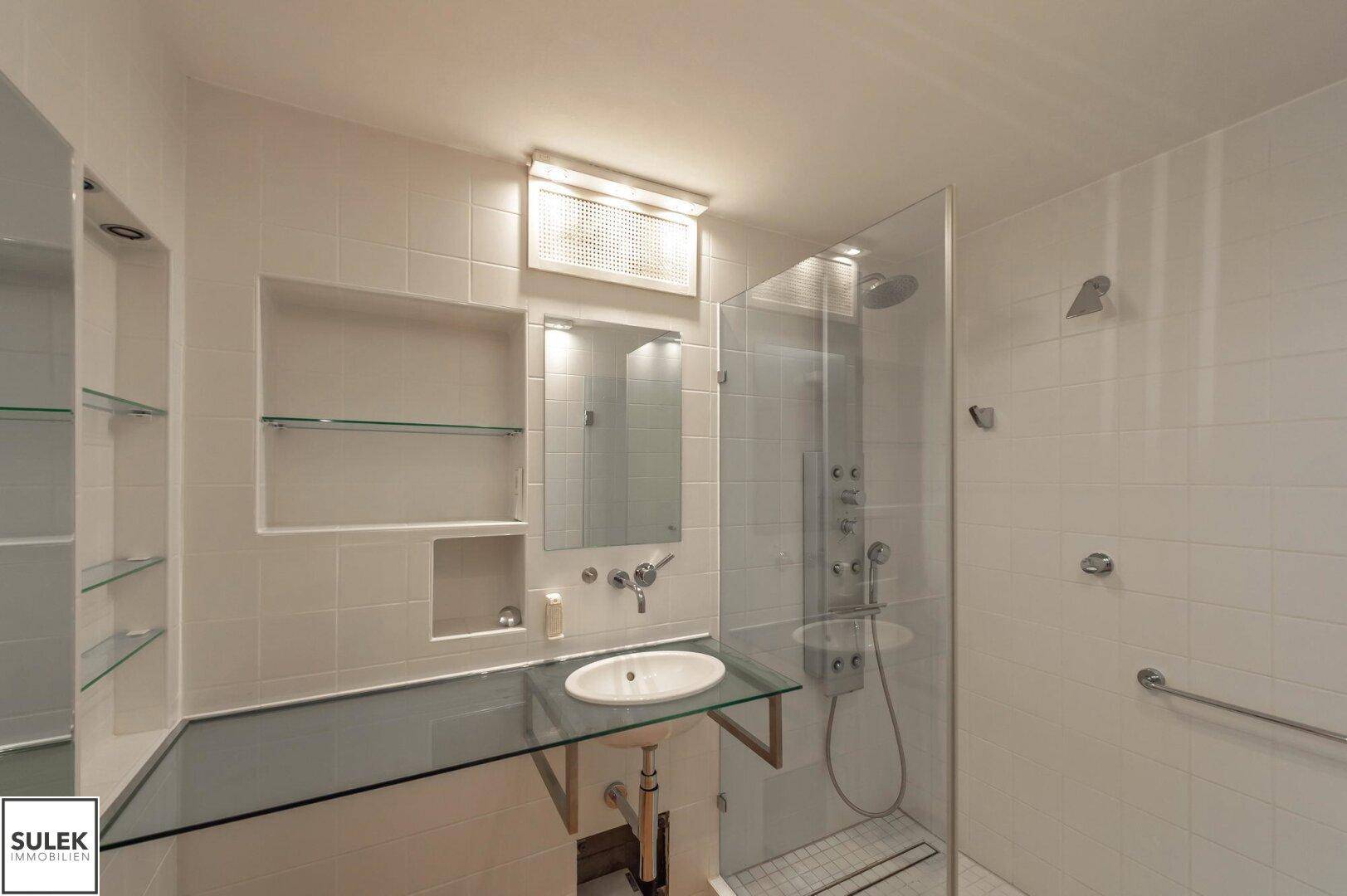 Modernes Badezimmer mit großer Duschkabine, Waschbecken und weißen Fliesen, sehr gepflegt und hell.