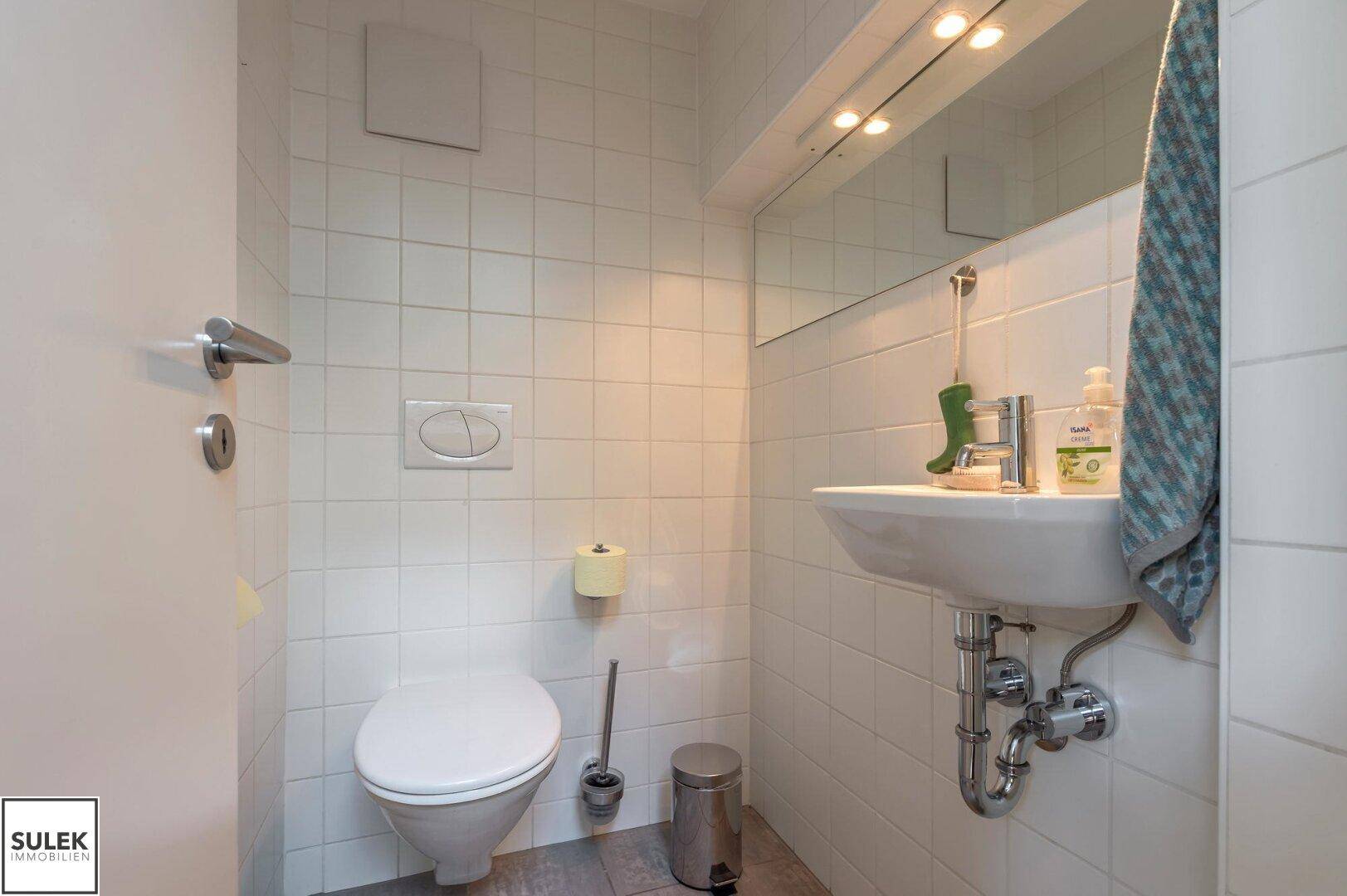 Kleines Gäste-WC mit wandhängender Toilette und Waschbecken in hellen Fliesen, funktional und sauber.