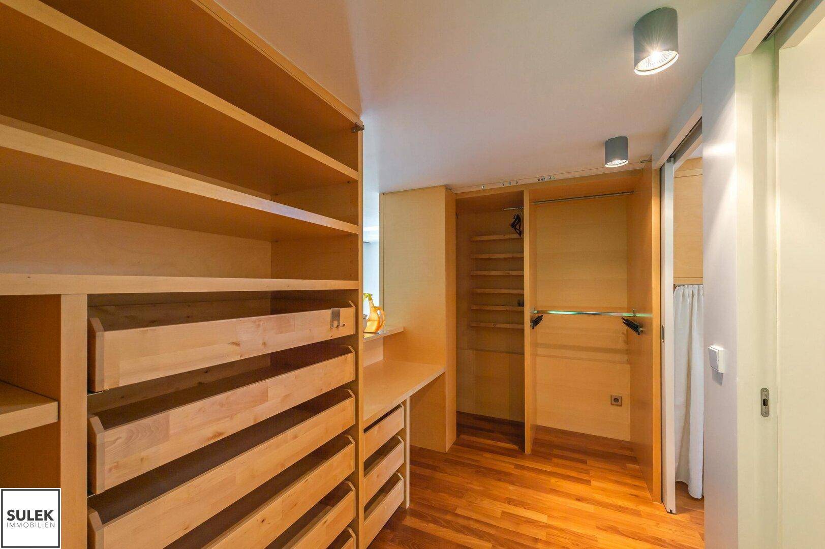 Geräumiger begehbarer Kleiderschrank mit vielen Ablagen und Schubladen aus hellem Holz, sehr praktisch.