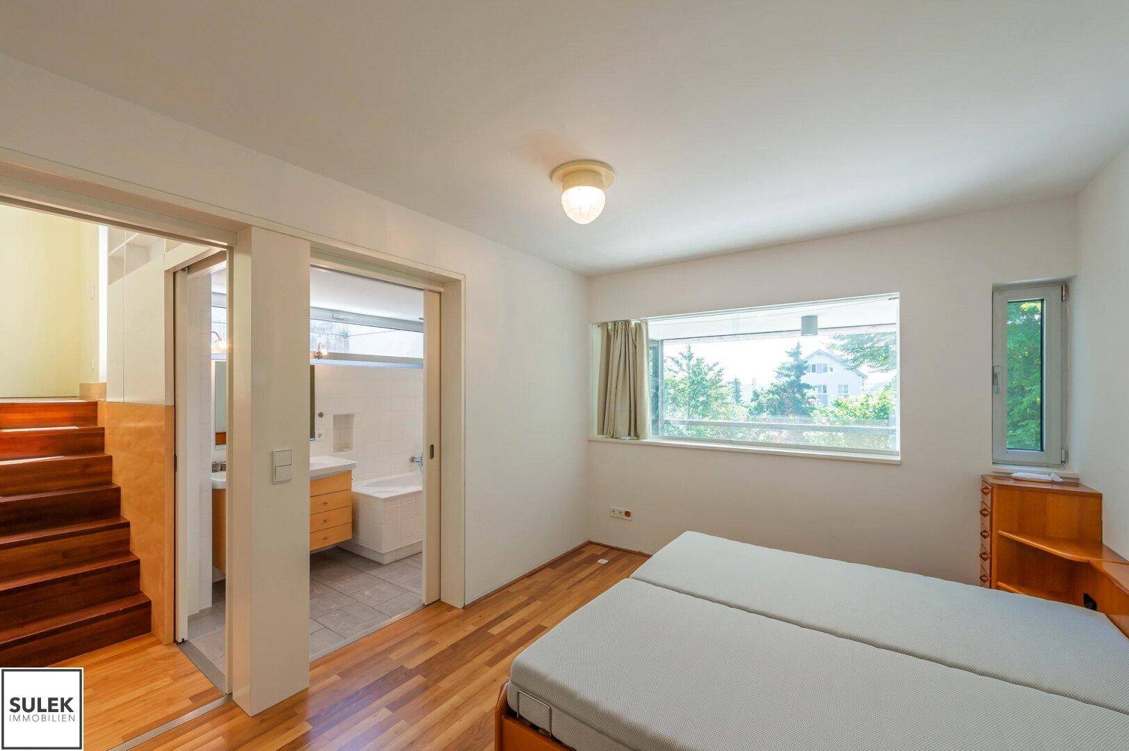 Schlafzimmer mit Holzboden, Bett und direktem Zugang zu einem modernen Badezimmer, sehr komfortabel.