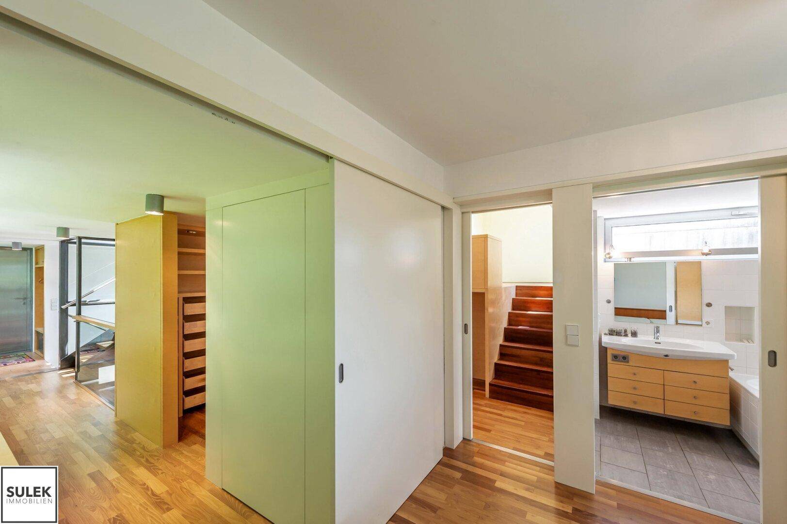 Flur mit Holzboden, Schiebetüren und Zugang zu Bad und begehbarem Kleiderschrank, gut durchdacht.
