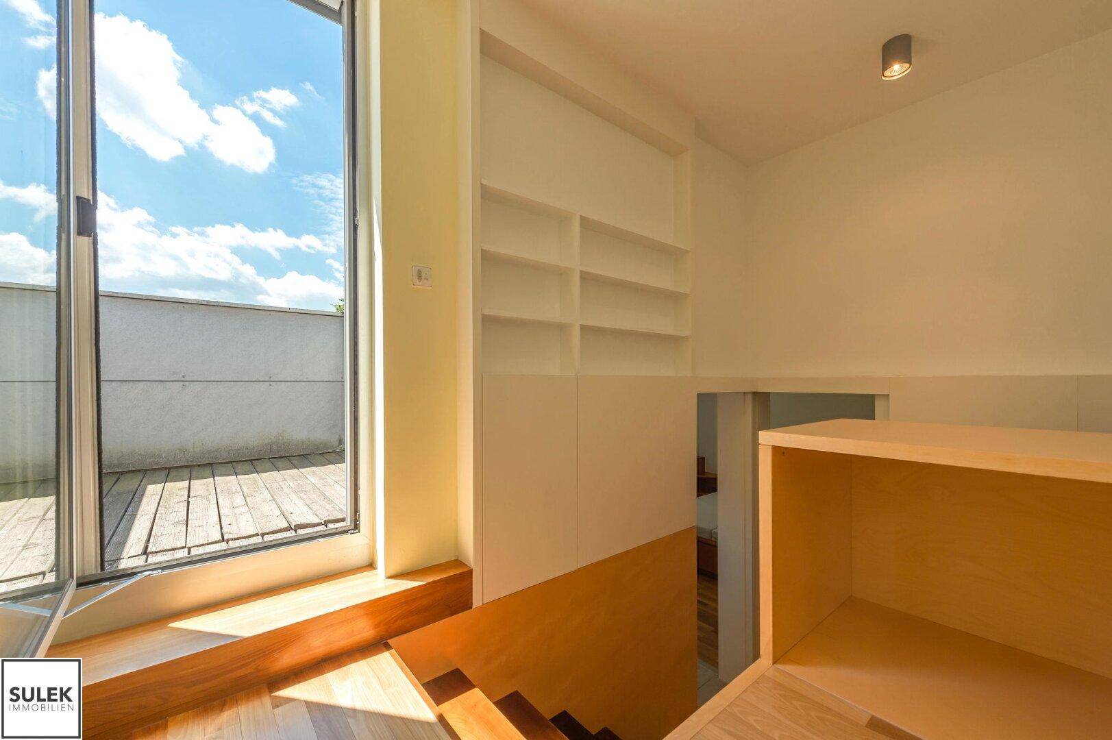 Heller Treppenabsatz mit Holzboden, Einbauregalen und Zugang zur Dachterrasse, sehr funktional.